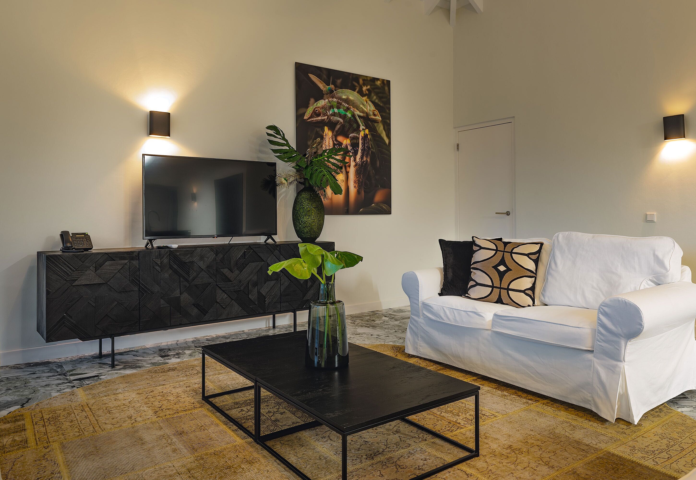 Una sala de estar moderna con una mesa de centro negra, un sofá blanco, un mueble negro y un televisor en la pared.