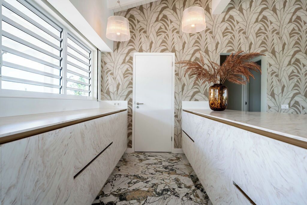 A bathroom with a white door, marble countertops, and a patterned wallpaper.