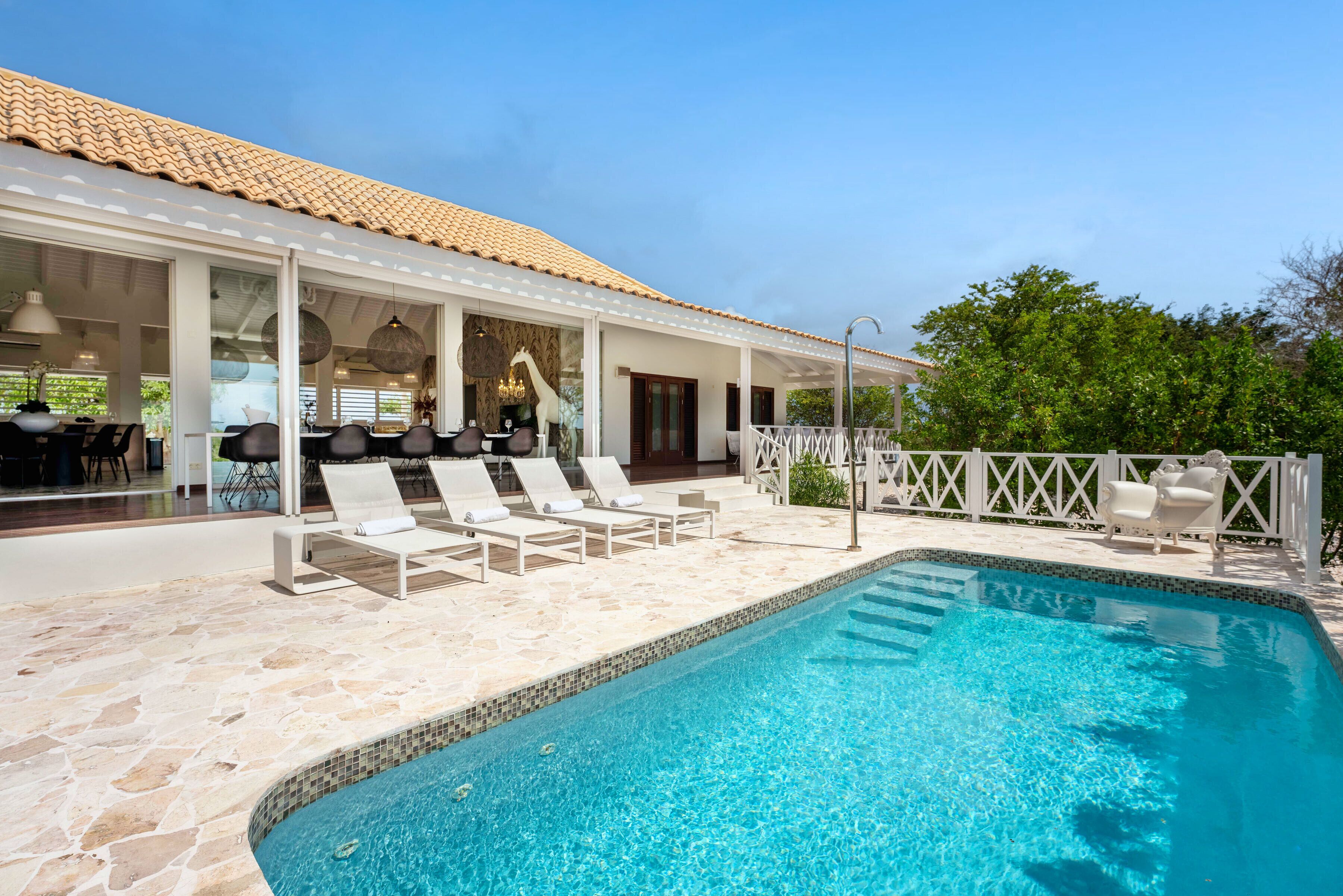 A pool area with lounge chairs, a covered seating area, and a tiled roof.