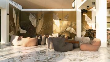 A spacious indoor area with a marble floor, multiple seating options including bean bags and sofas, and a decorative wall with leaf patterns.