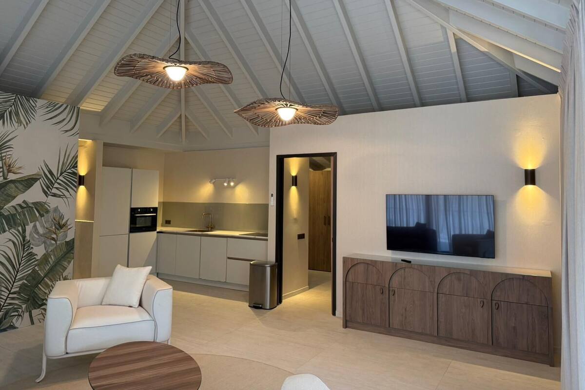 Un interior moderno con sofá, televisor, mueble de madera, cocina y ventilador de techo.