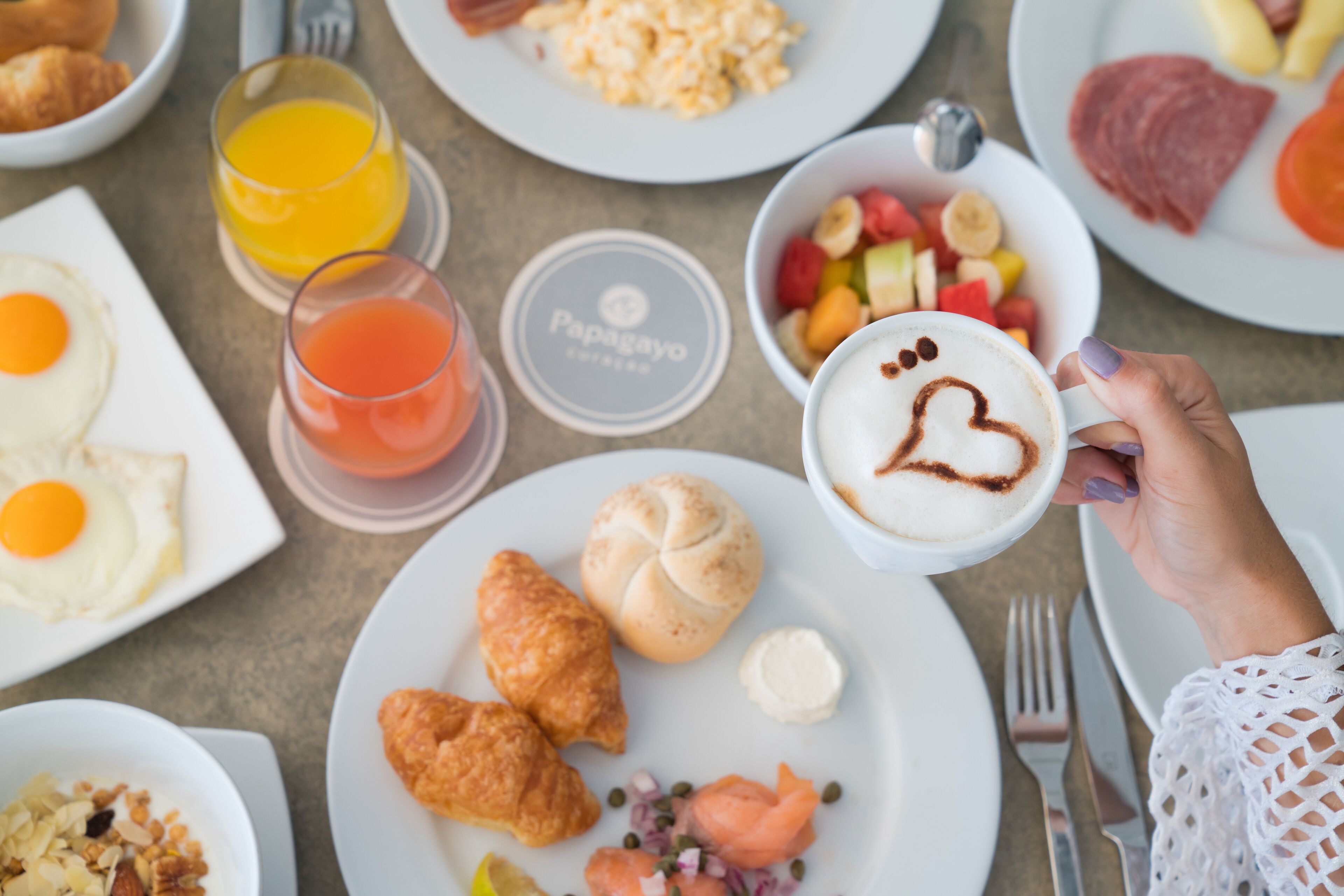 A breakfast setting with various dishes including eggs, croissants, and a coffee cup with a heart design.