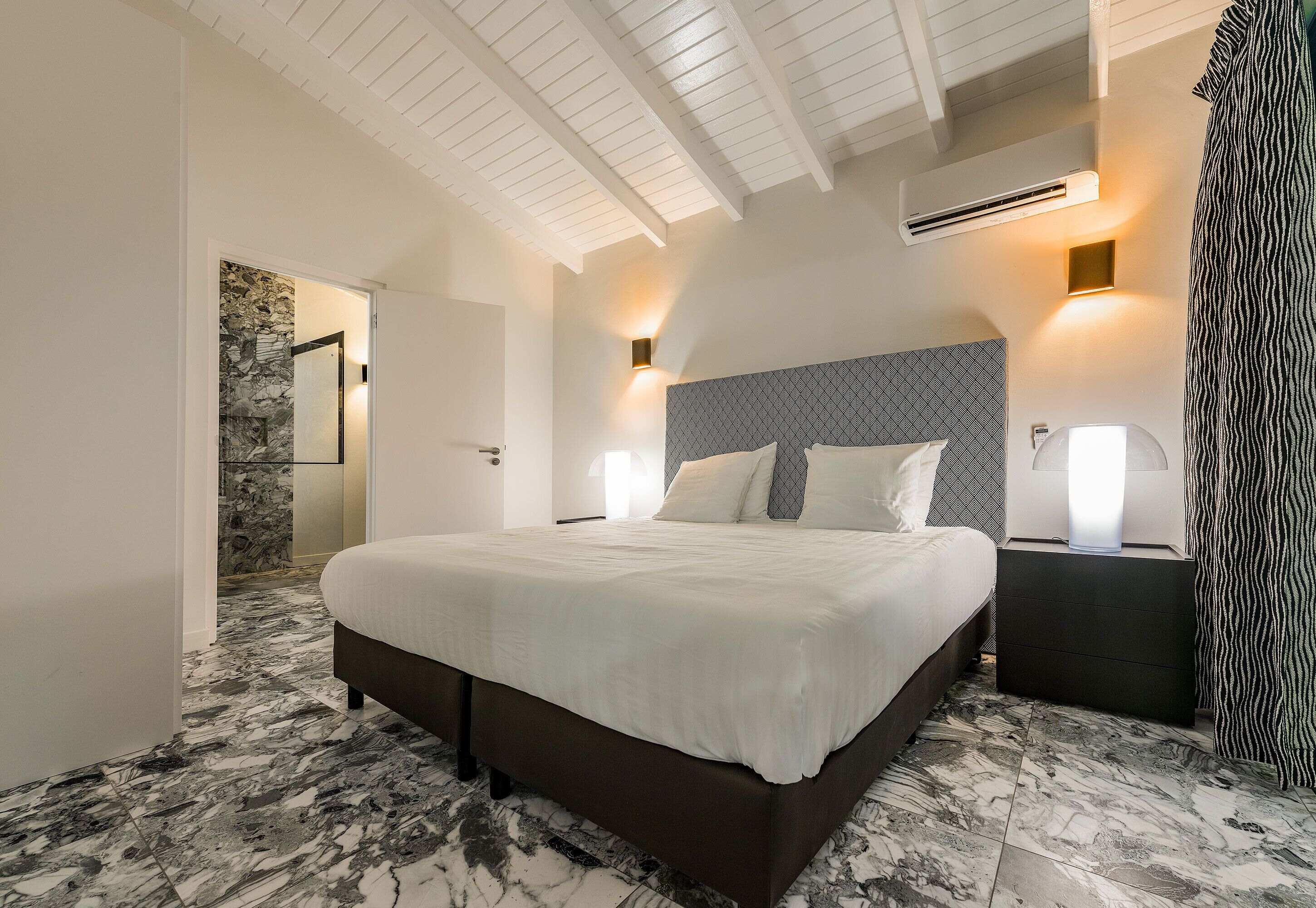Un dormitorio con una cama grande, suelo de mármol, cabecero moderno e iluminación empotrada.