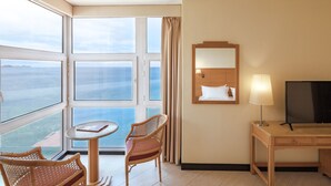 Habitación de hotel con balcón, una cama, televisor, escritorio y dos sillas de mimbre.