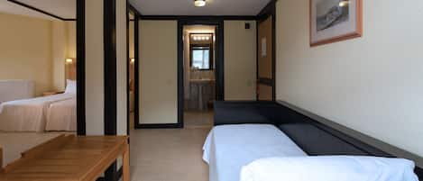 A hotel room with two beds, a wooden table, and a bathroom visible through an open door.