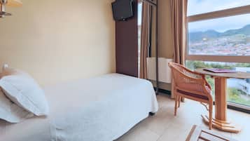 Una habitación de hotel con una cama, un televisor montado en un mueble de madera, una mesa con una silla y un ventanal con vistas a la ciudad.
