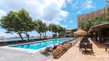 Relax by the ocean-view pool surrounded by lounge chairs and umbrellas, with a building in the background.