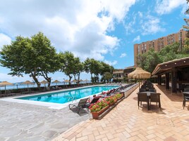 Un área junto a la piscina con sillones de descanso, una piscina y un edificio al fondo.