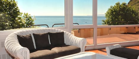 A white wicker sofa with black cushions and a matching table on a terrace with a view of the sea.