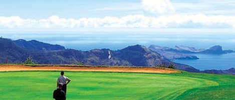 A person standing on a golf course with a view of mountains and the sea in the background.
