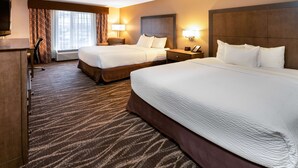 A hotel room with two beds, a desk, a TV, and a window with curtains.
