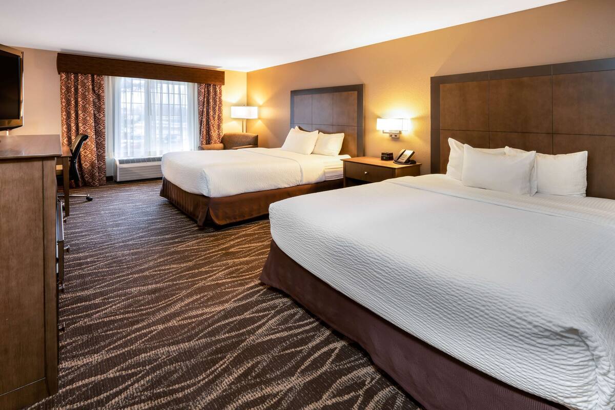 A hotel room with two beds, a desk, a TV, and a window with curtains.