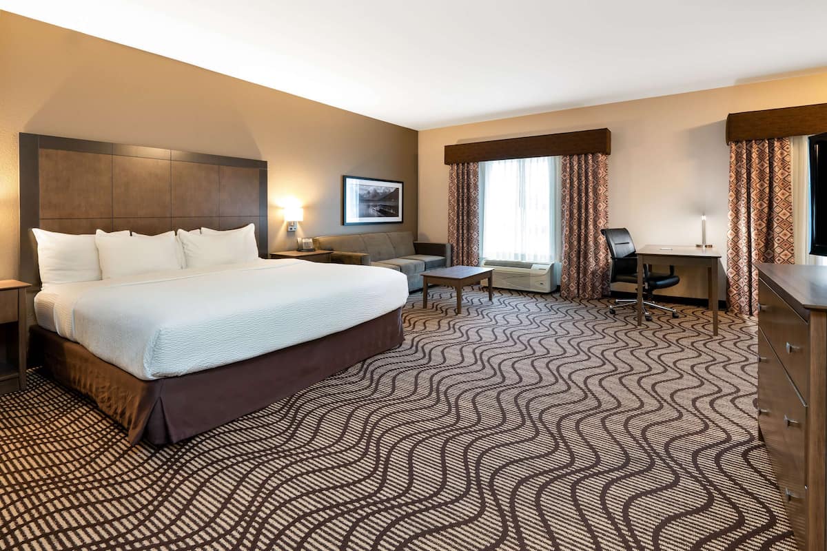 A hotel room with a large bed, a desk, a chair, and a small table.