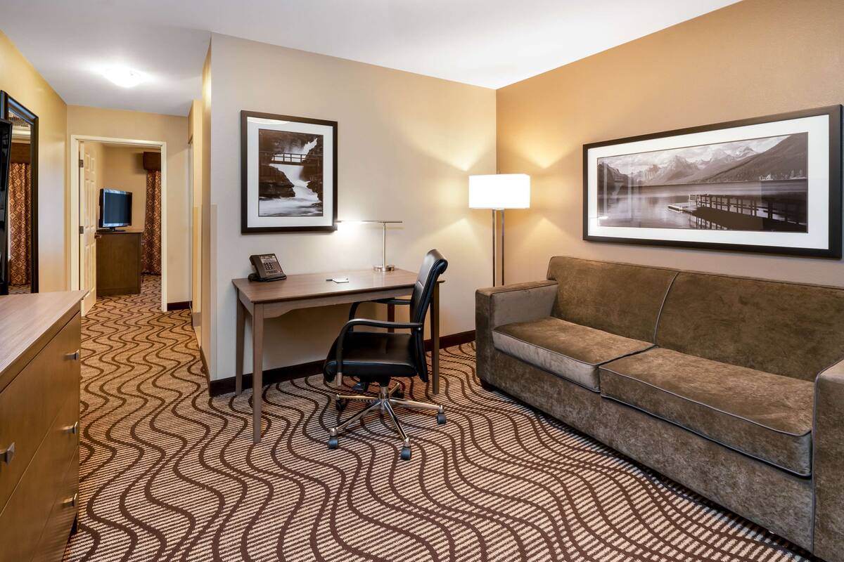 A hotel room with a desk, a chair, a sofa, a TV, and two framed pictures on the wall.