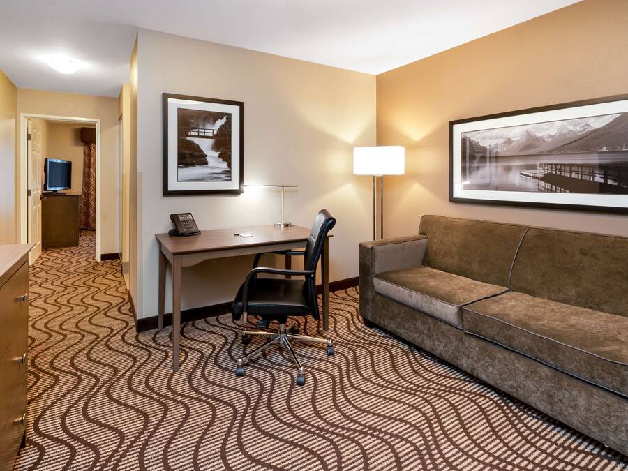 Habitación de hotel con escritorio, una silla, sofá, televisor y dos cuadros en la pared.