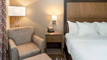 A hotel room with a bed, a nightstand with a lamp, a chair, and a small table.