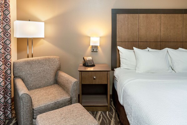 A hotel room with a bed, a nightstand with a lamp, a chair, and a small table.