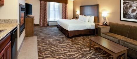 A hotel room with a bed, a sofa, a coffee table, a TV, and a fireplace.