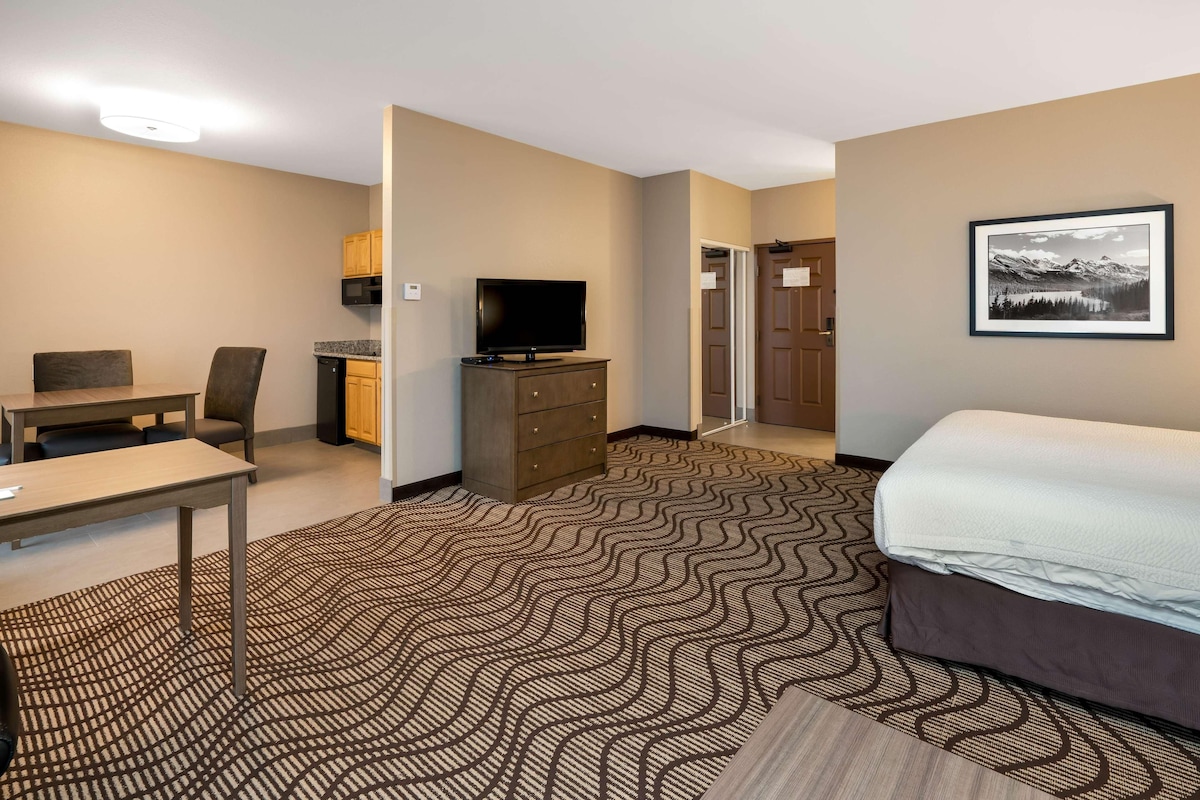 A hotel room with a bed, a desk, a television, a dresser, and a door leading to another room.