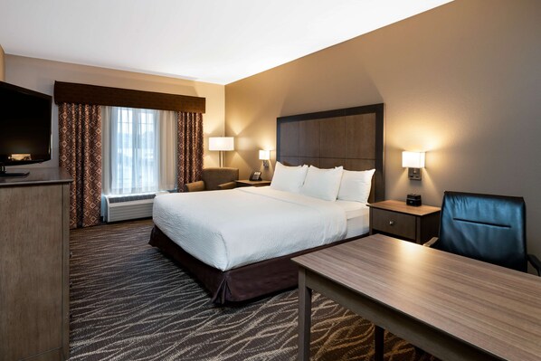 A hotel room with a large bed, bedside tables with lamps, a desk, a chair, and a TV.