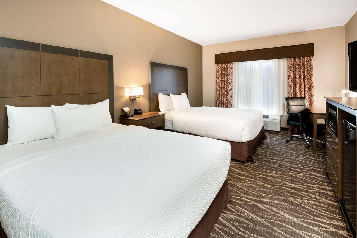 A hotel room with two beds, a desk, a chair, a television, and a window with curtains.