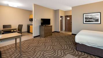 A hotel room with a bed, a desk with a chair, a television on a dresser, and a patterned carpet.