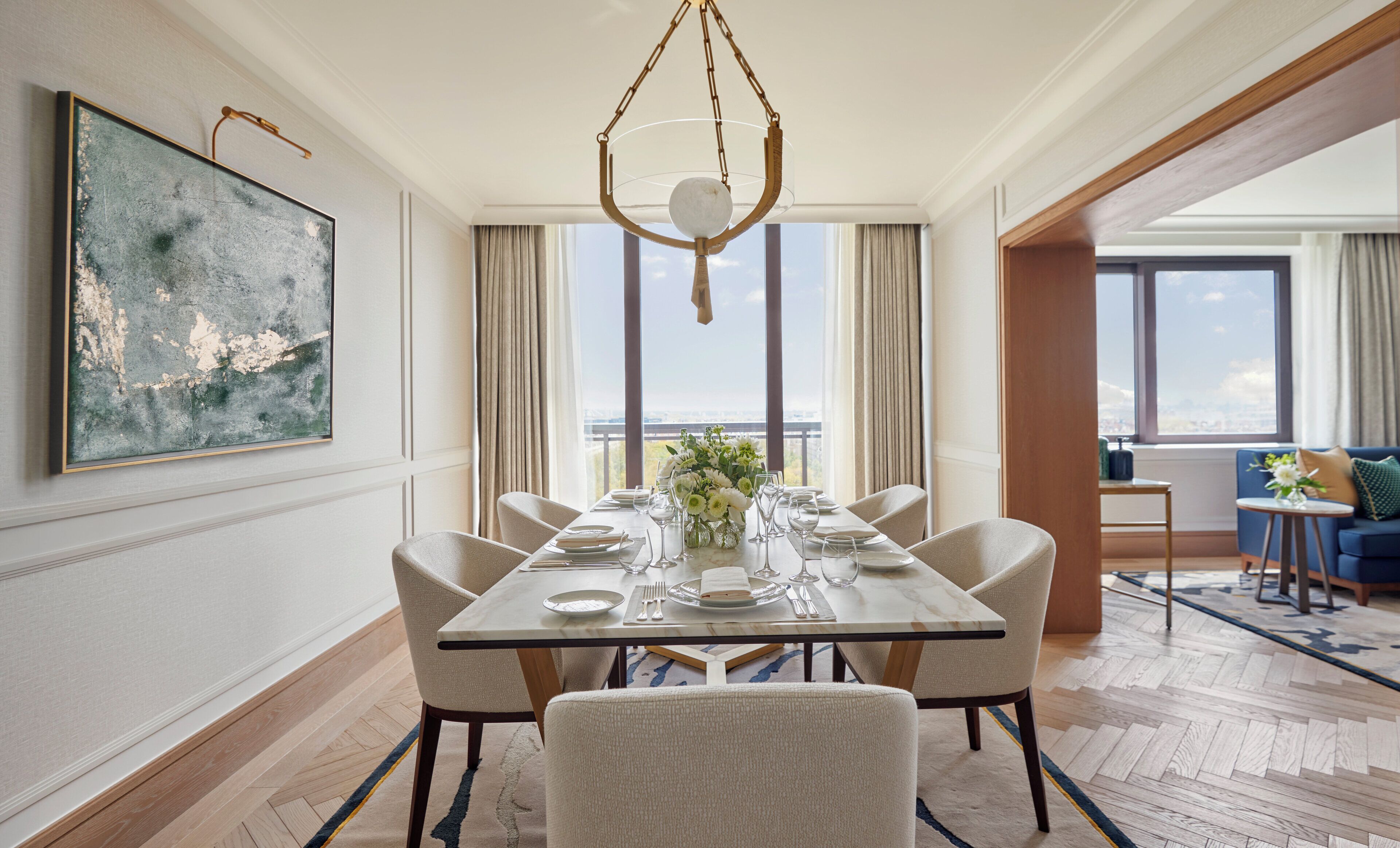 A dining area with a table set for six, a hanging light fixture, and a large abstract painting on the wall.