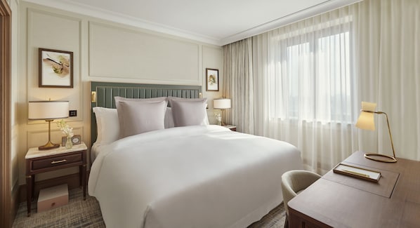 A hotel room with a large bed, a bedside table with a lamp, a chair, and a desk with a lamp. - Jumeirah Carlton Tower London (London)