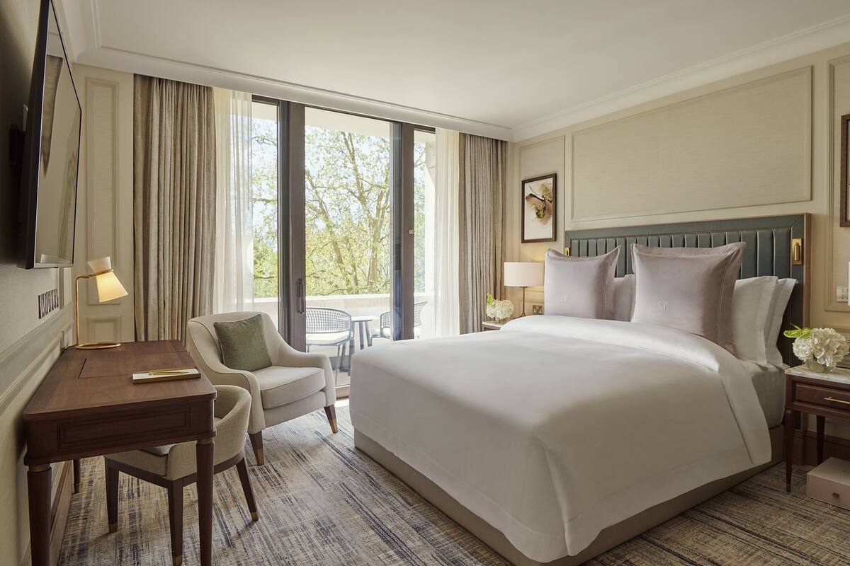Habitación de hotel con una cama grande, un escritorio, una silla y vistas al exterior.