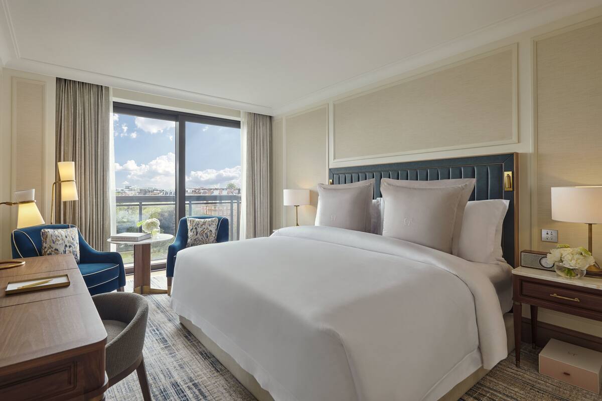 Habitación de hotel con una cama grande, un escritorio, una silla y vistas a la ciudad a través de la ventana.