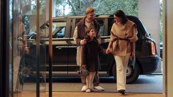 A family holding hands in front of a black SUV, with a glass door reflecting a person inside.