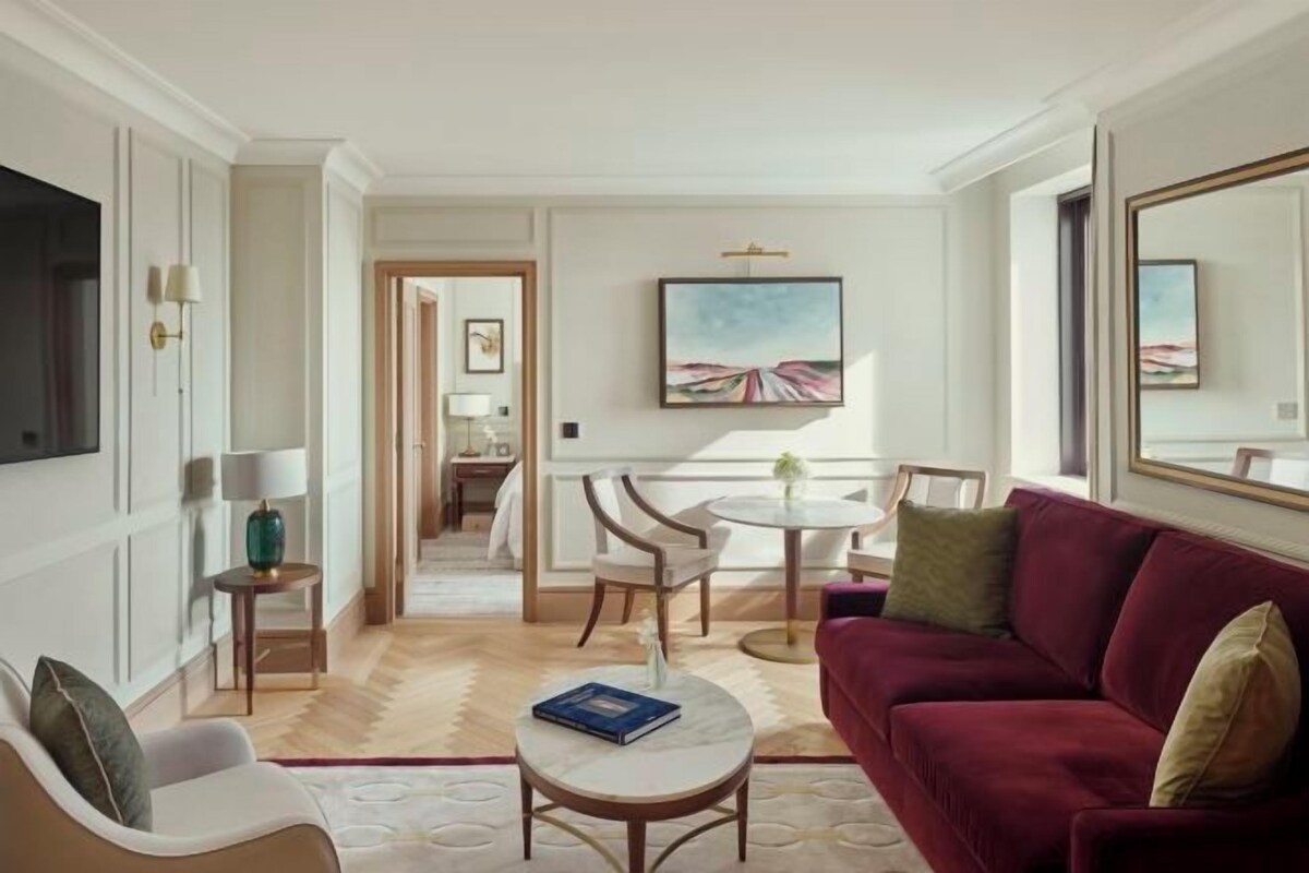 A hotel room with a red sofa, a round coffee table, a TV, and a painting on the wall.