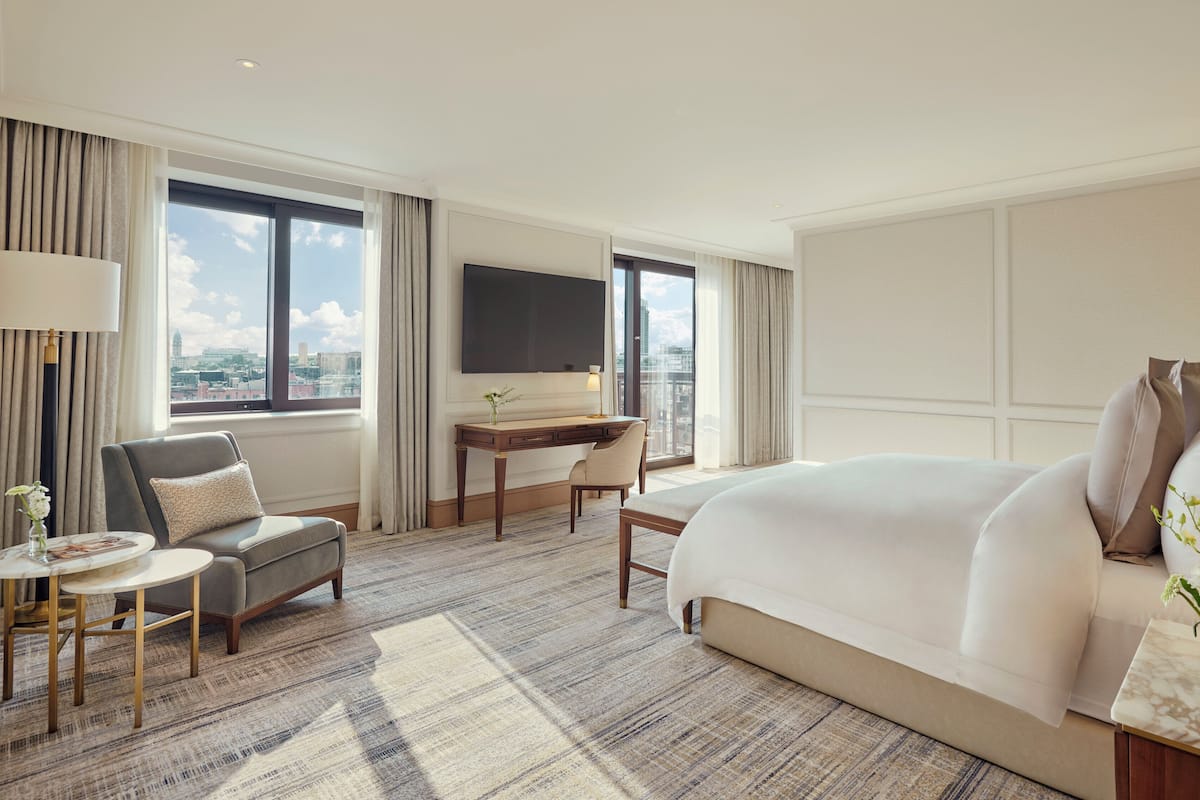 Habitación de hotel con una cama grande, un escritorio, una silla, una mesita y un televisor.