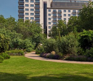 Un jardín cuidado con un sendero curvo que conduce a un edificio moderno con varios balcones y ventanas amplias.