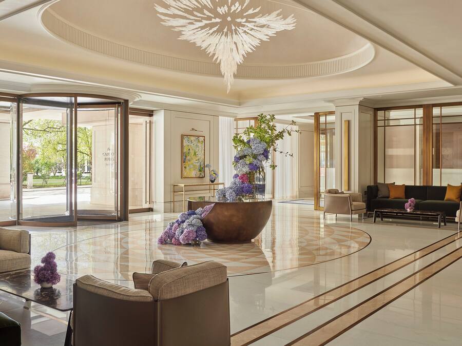 A spacious lobby with a large, ornate chandelier, a central floral arrangement, and a seating area with sofas and armchairs.