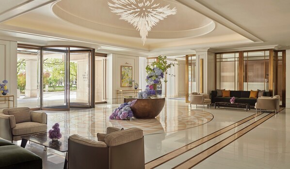 Un vestíbulo espacioso con una gran araña ornamentada, un arreglo floral central y un área de descanso con sofás y sillones.