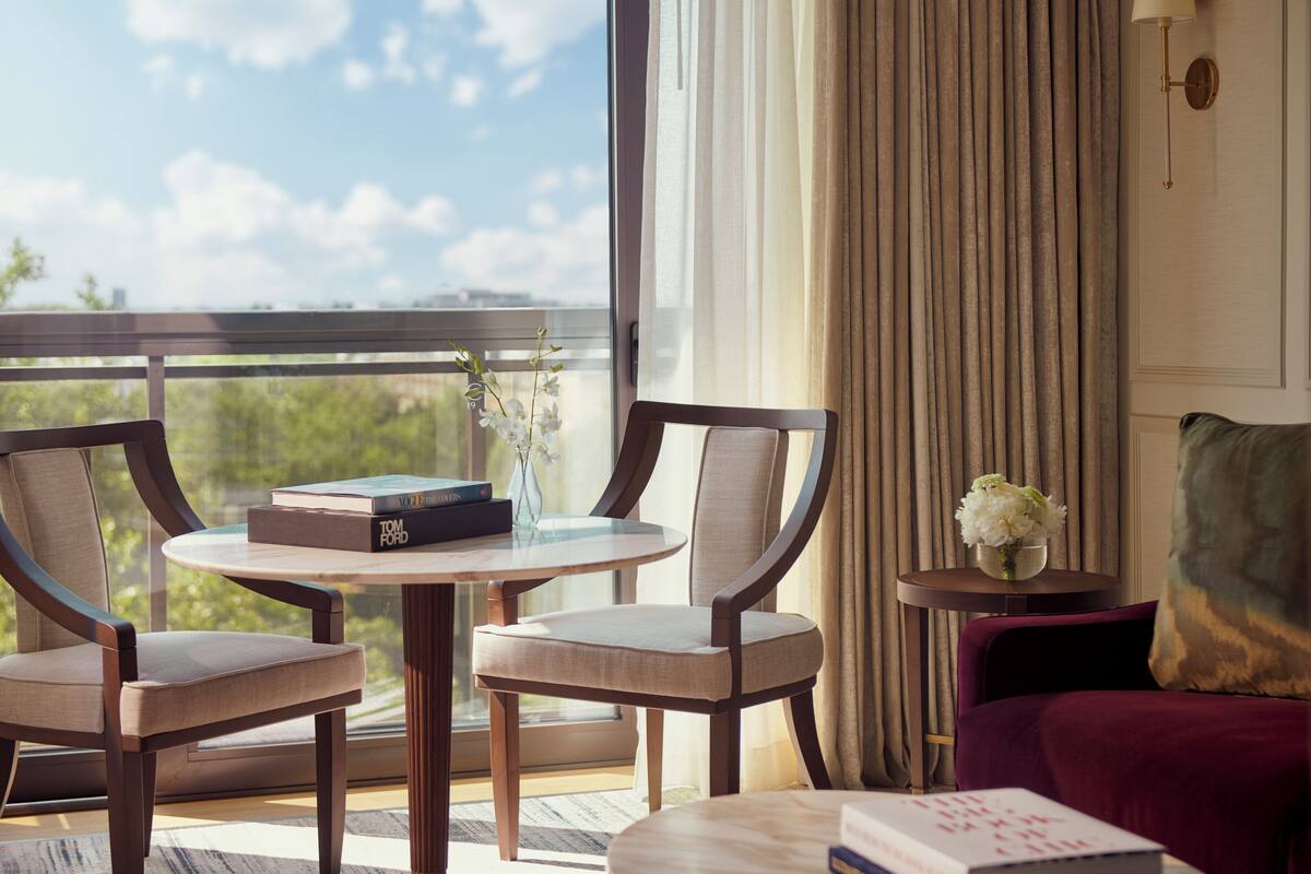 Una habitación con dos sillones, una mesita, un sofá, un jarrón con flores y vistas al exterior.