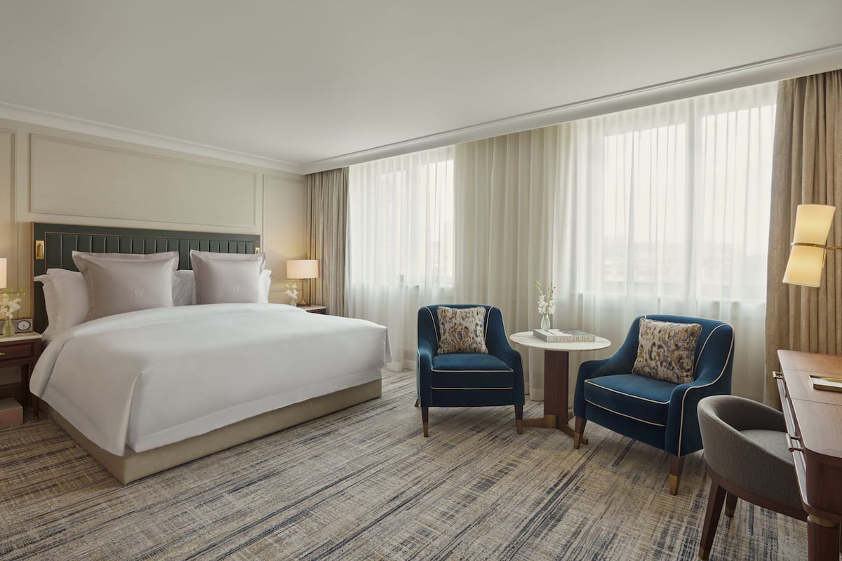Una habitación de hotel con una cama grande, dos sillones, una mesita y un escritorio con lámparas.