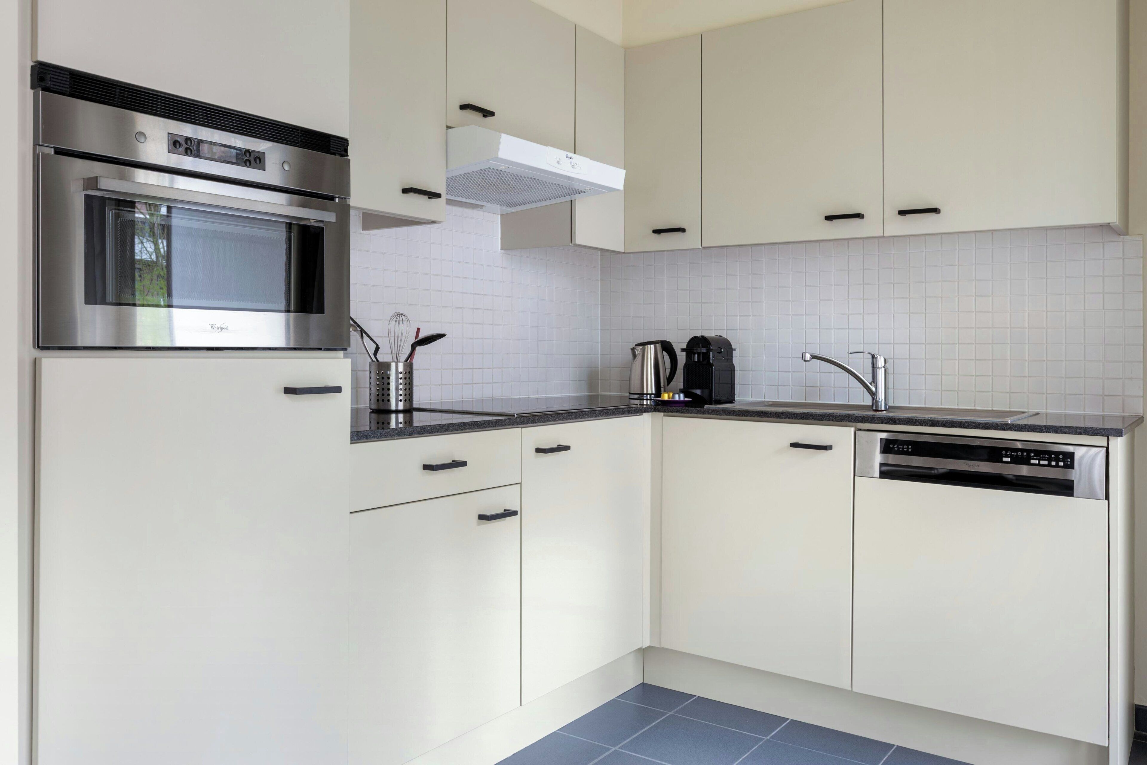 Una cocina moderna con electrodomésticos de acero inoxidable, armarios blancos y salpicadero de azulejos.