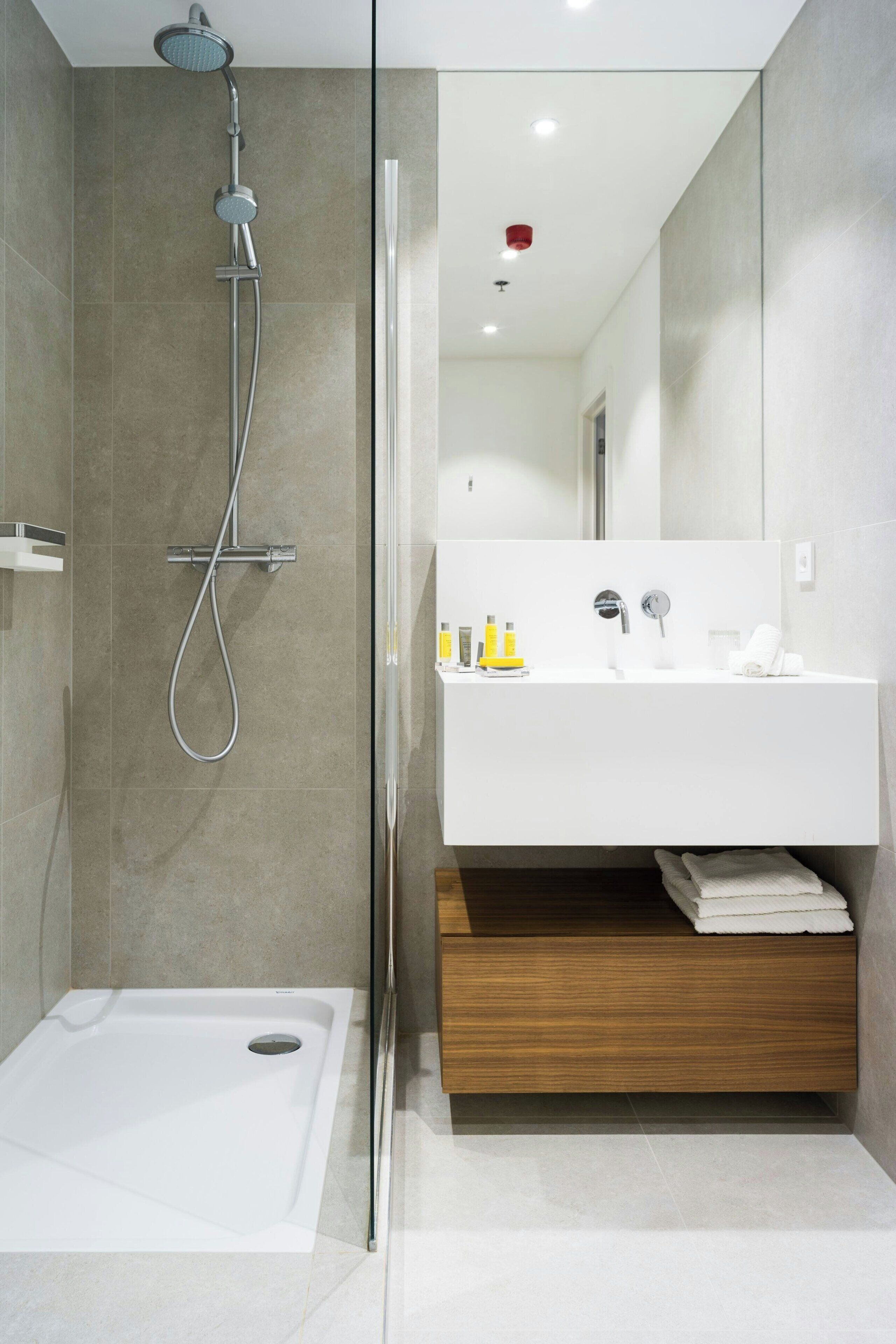 Een moderne badkamer met een douche, wastafel en spiegel.