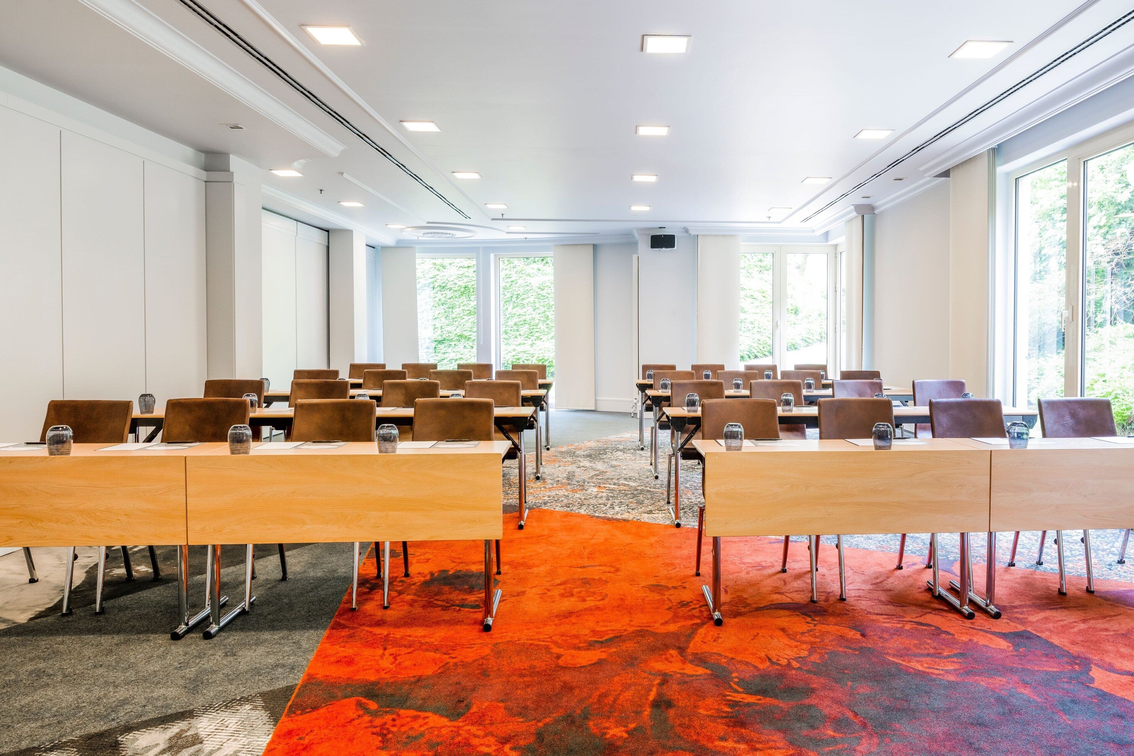 Un salón de conferencias con varias mesas y sillas, ventanas amplias y alfombra roja.
