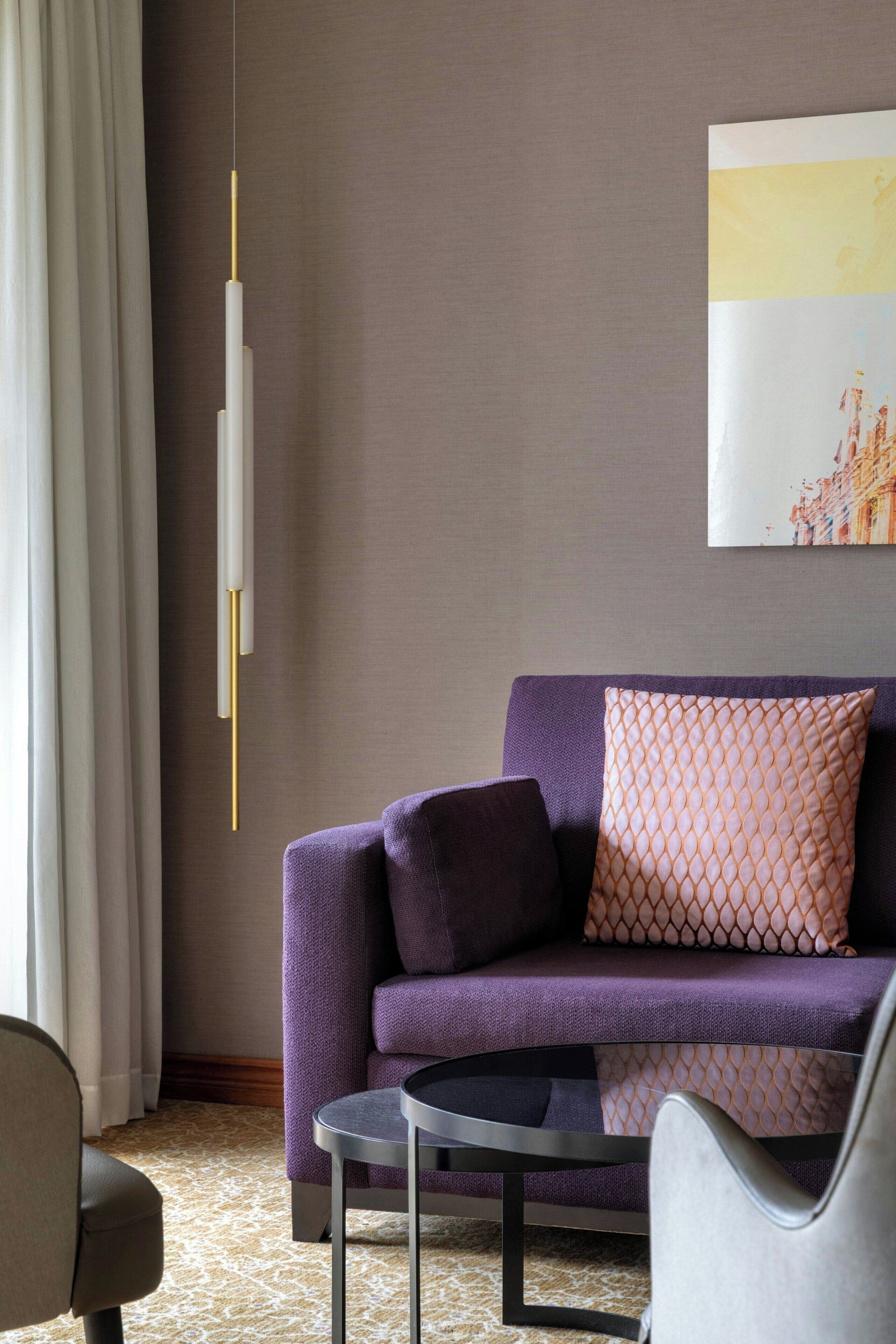 A modern living room with a purple sofa, a round coffee table, and a hanging light fixture.