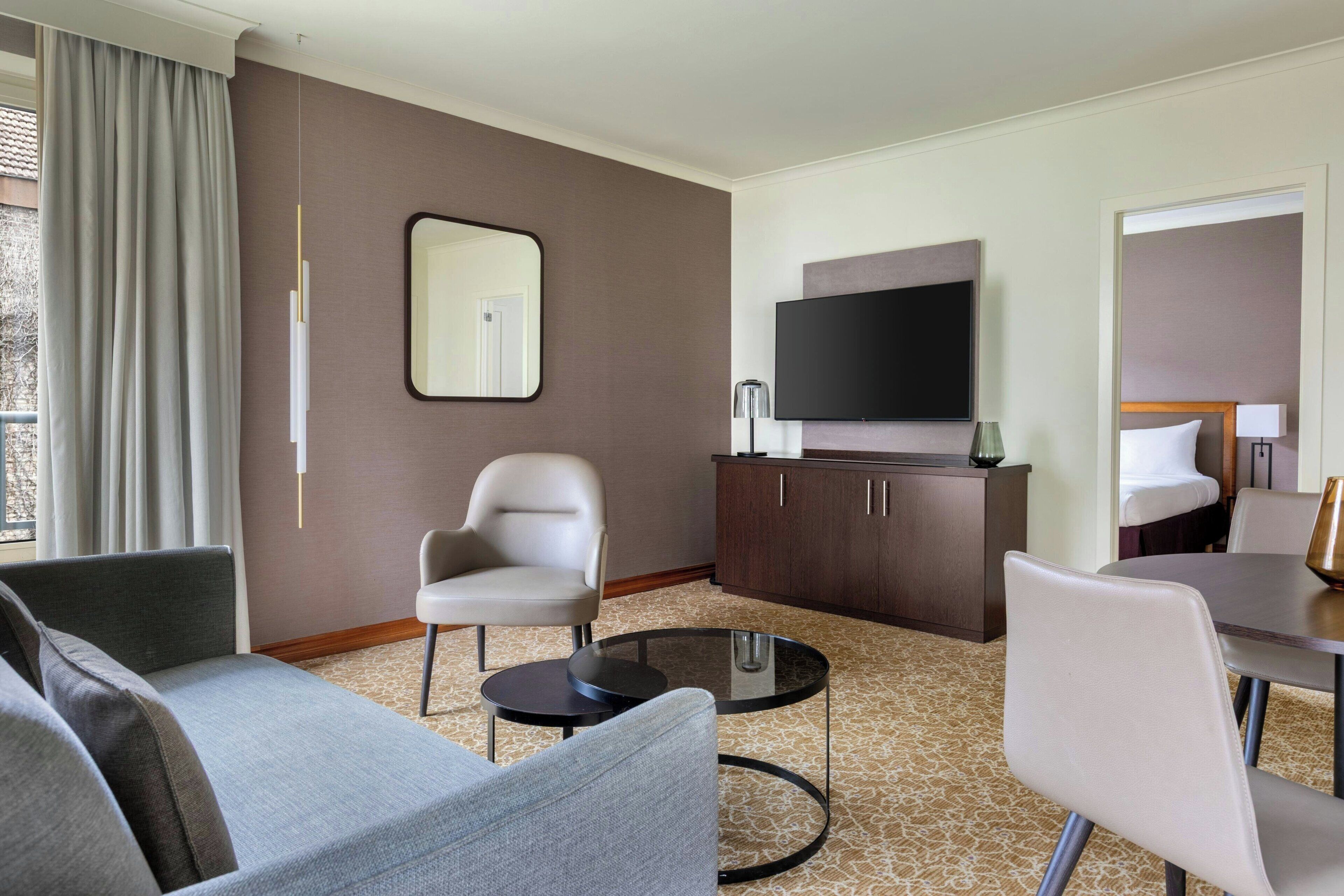 Habitación de hotel con sofá, sillón, televisor y escritorio con lámpara.