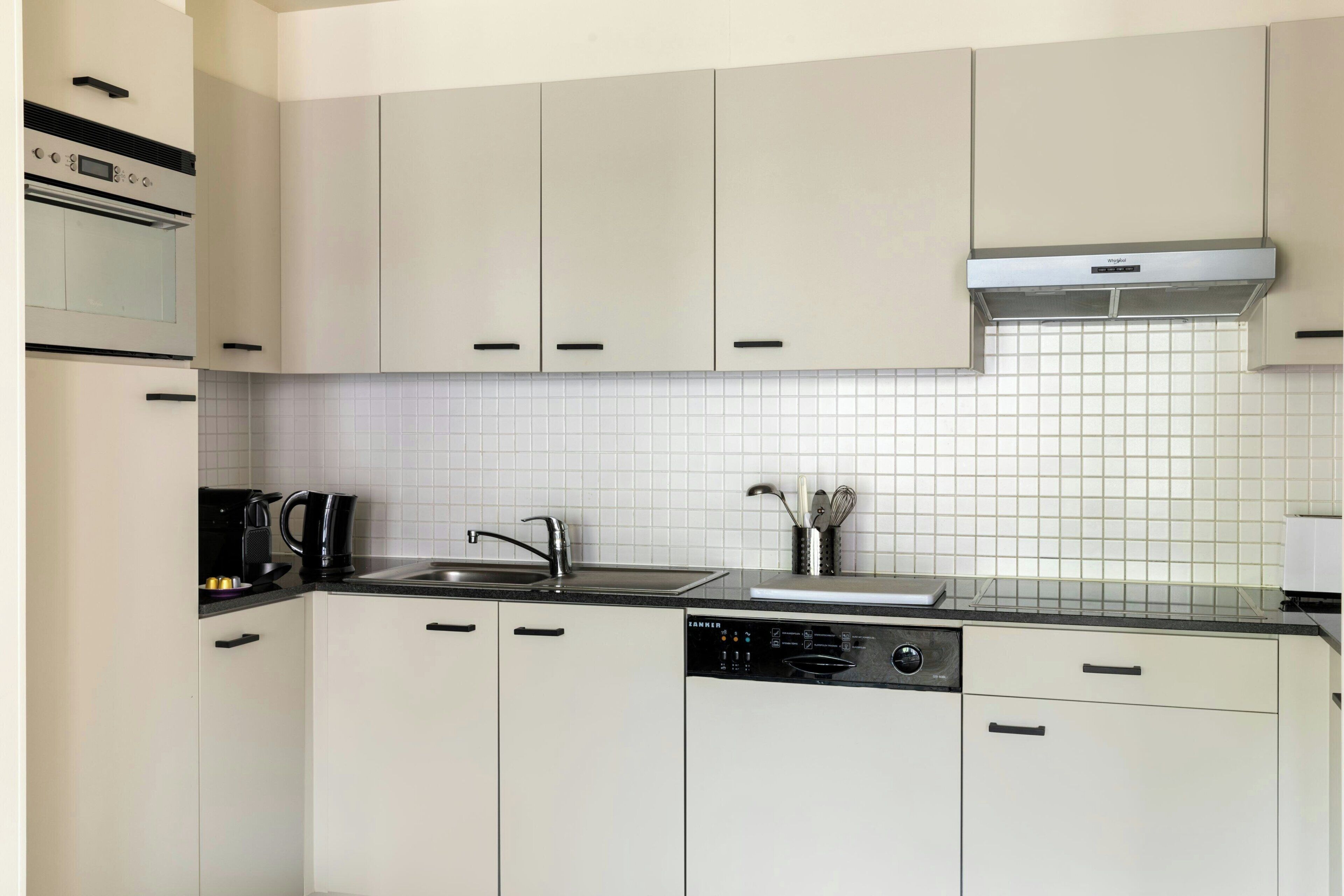 Una cocina moderna con armarios blancos, un lavamanos de acero inoxidable y un lavavajillas.