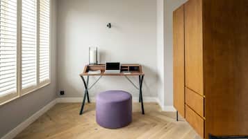 A room with a wooden desk, a purple ottoman, and a wardrobe.