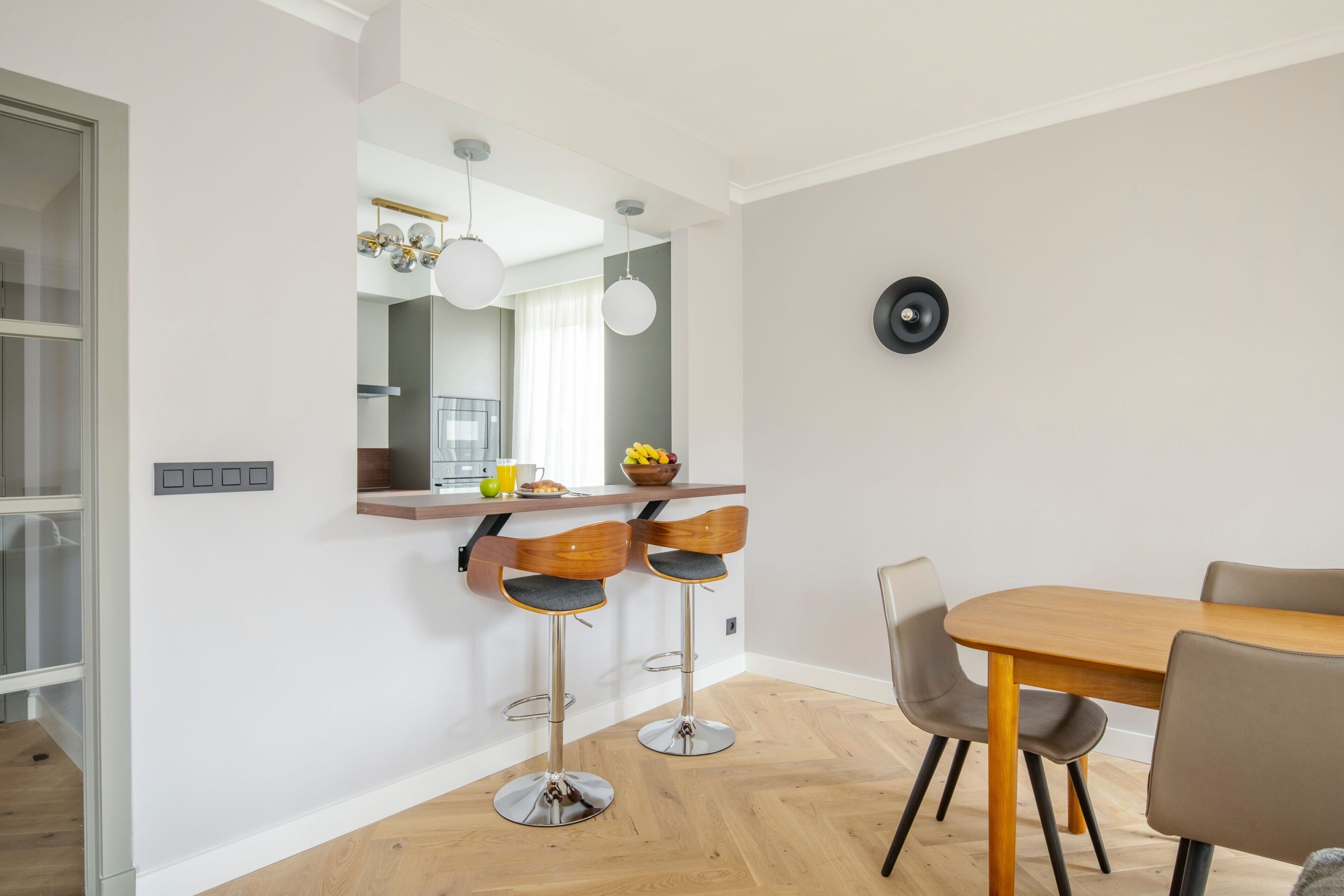 Een moderne keuken met een houten aanrecht, twee barkrukken, een eettafel met stoelen en een grote spiegel boven het aanrecht.