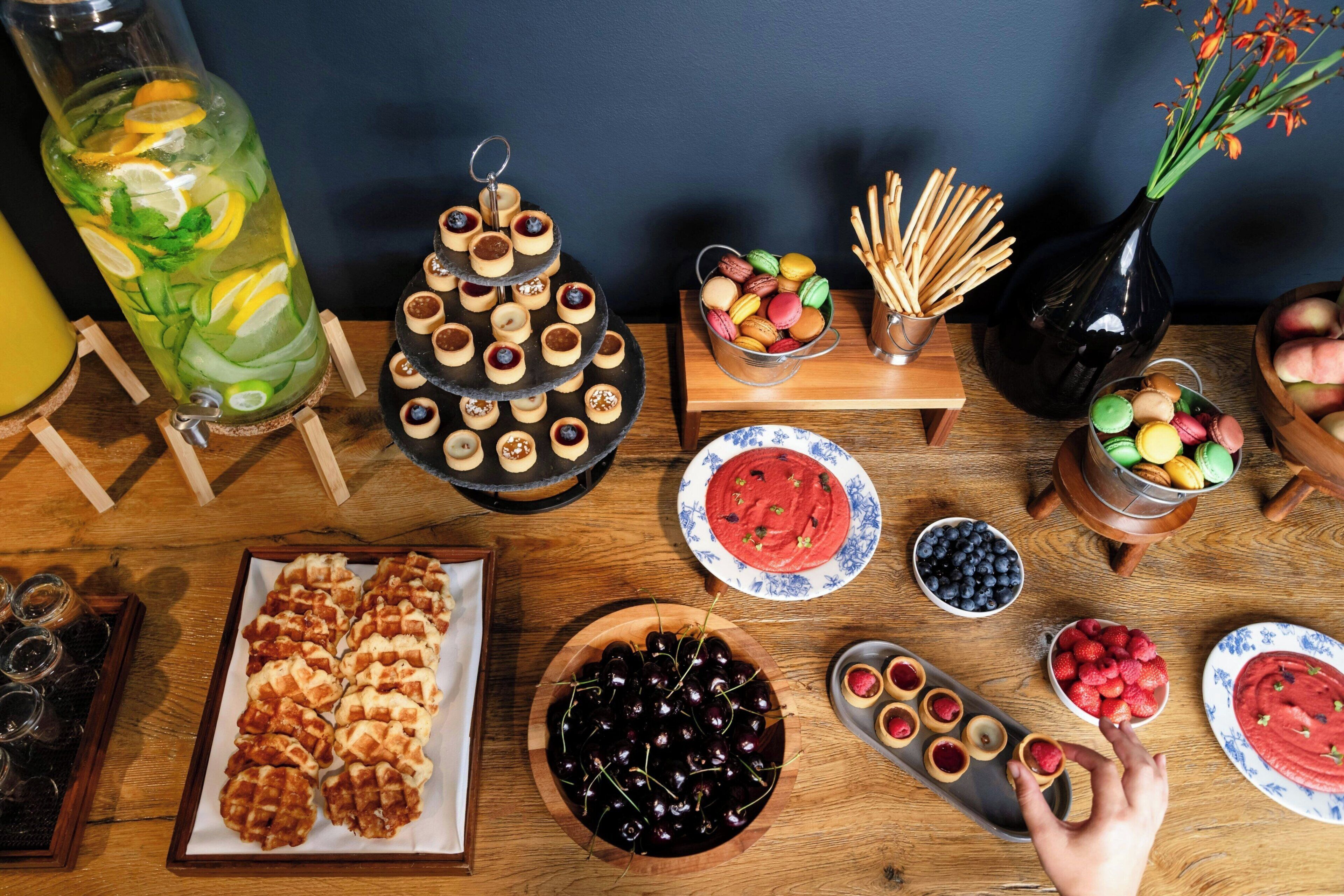 Une table sur laquelle on trouve divers aliments, notamment des macarons, des tartes et un grand verre de limonade.