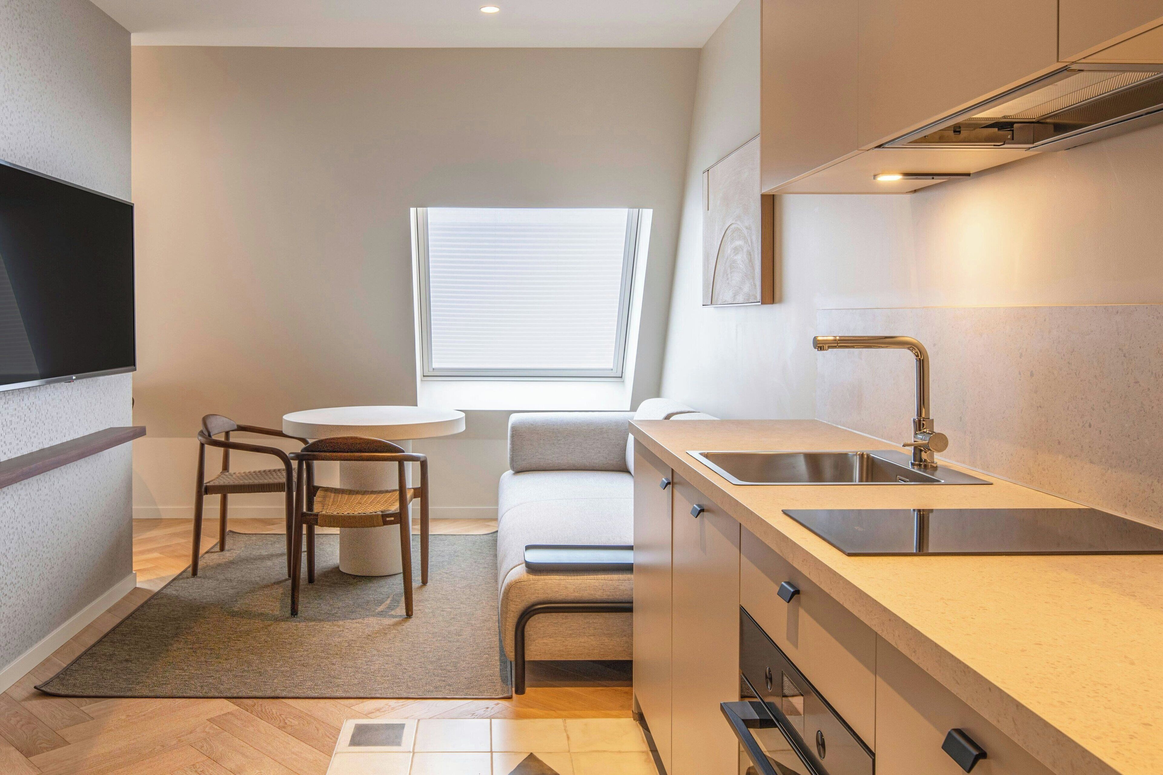 Una cocina compacta con estufa integrada, un lavamanos y un pequeño comedor con mesa y sillas.