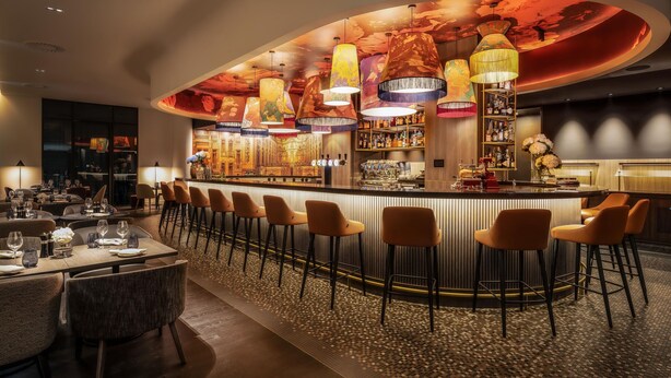 A bar area with a curved counter, multiple bar stools, and a variety of bottles and glasses on shelves. - Marriott Executive Apartments Brussels, European Quarter (Brussels)