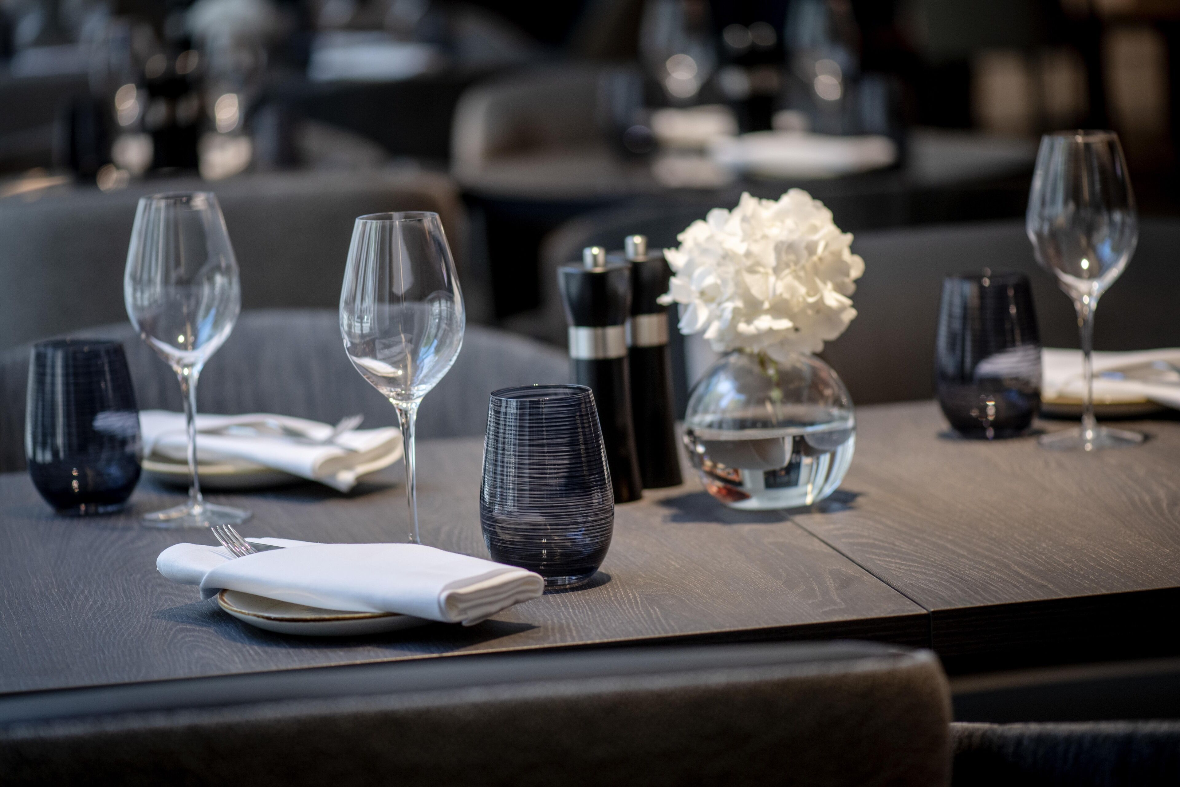 Una mesa de comedor dispuesta con copas de vino, platos y un florero con flores blancas.